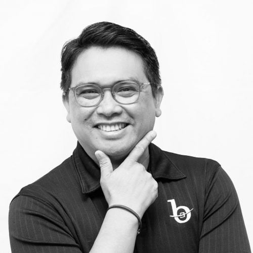 Black and white photo of a man with glasses and his hand in an L shape around his chin.