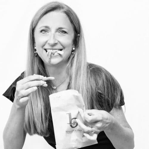 A woman eating french fries and smiling with them stuck in her teeth.
