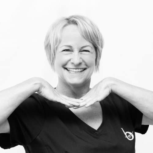 A black and white photo of a woman smiling with her hands underneath her chin.