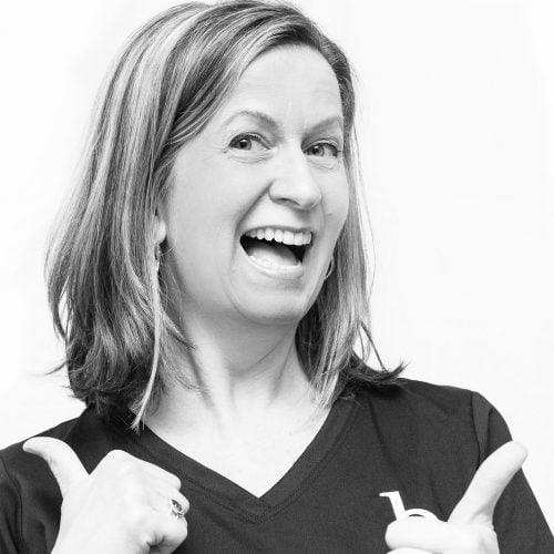 A black and white photo of a woman smiling and with a double-thumbs up.