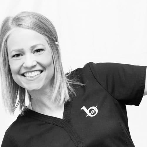 A black and white photo of a blonde woman smiling and leaning to the side.