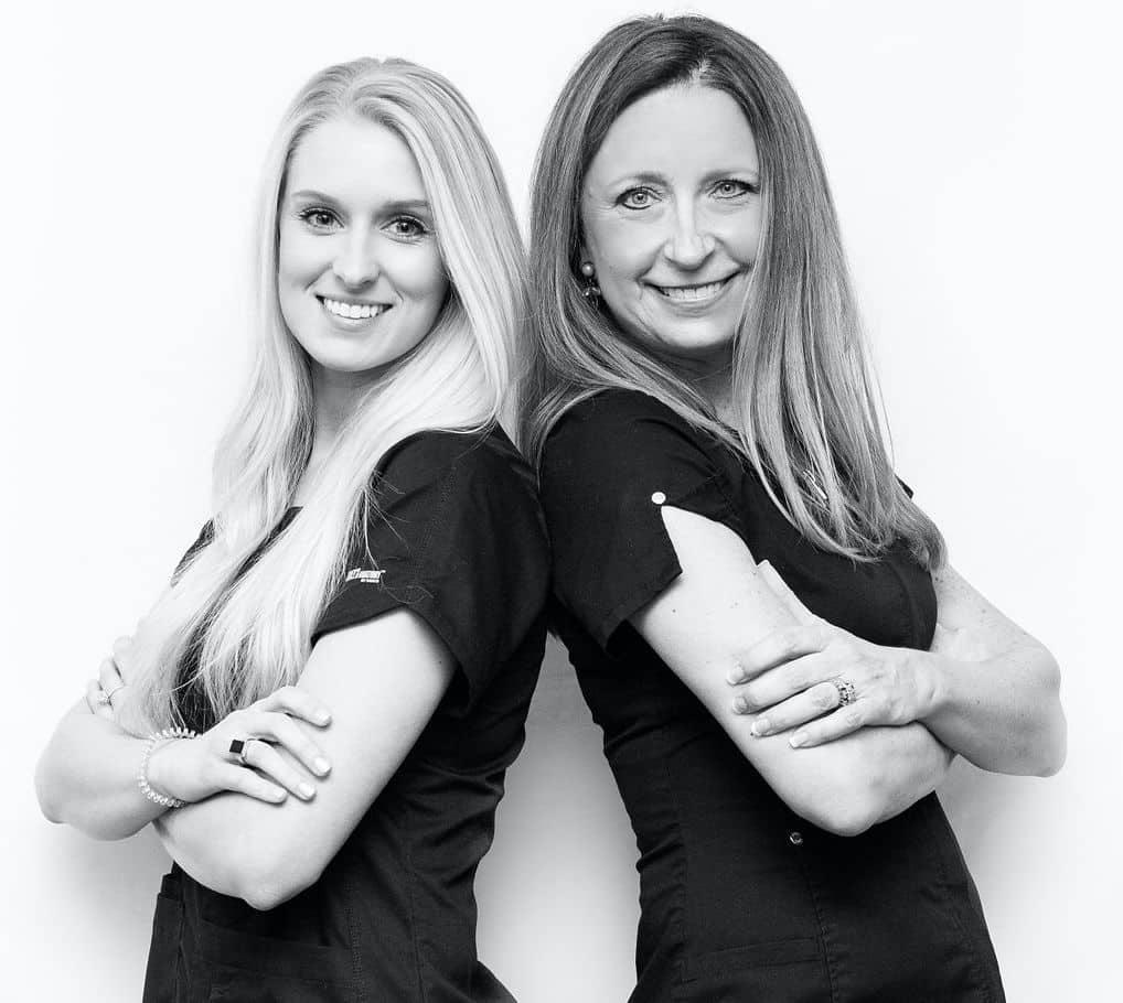 Black and white photo of a young blonde woman and an older blonde woman standing back to back.