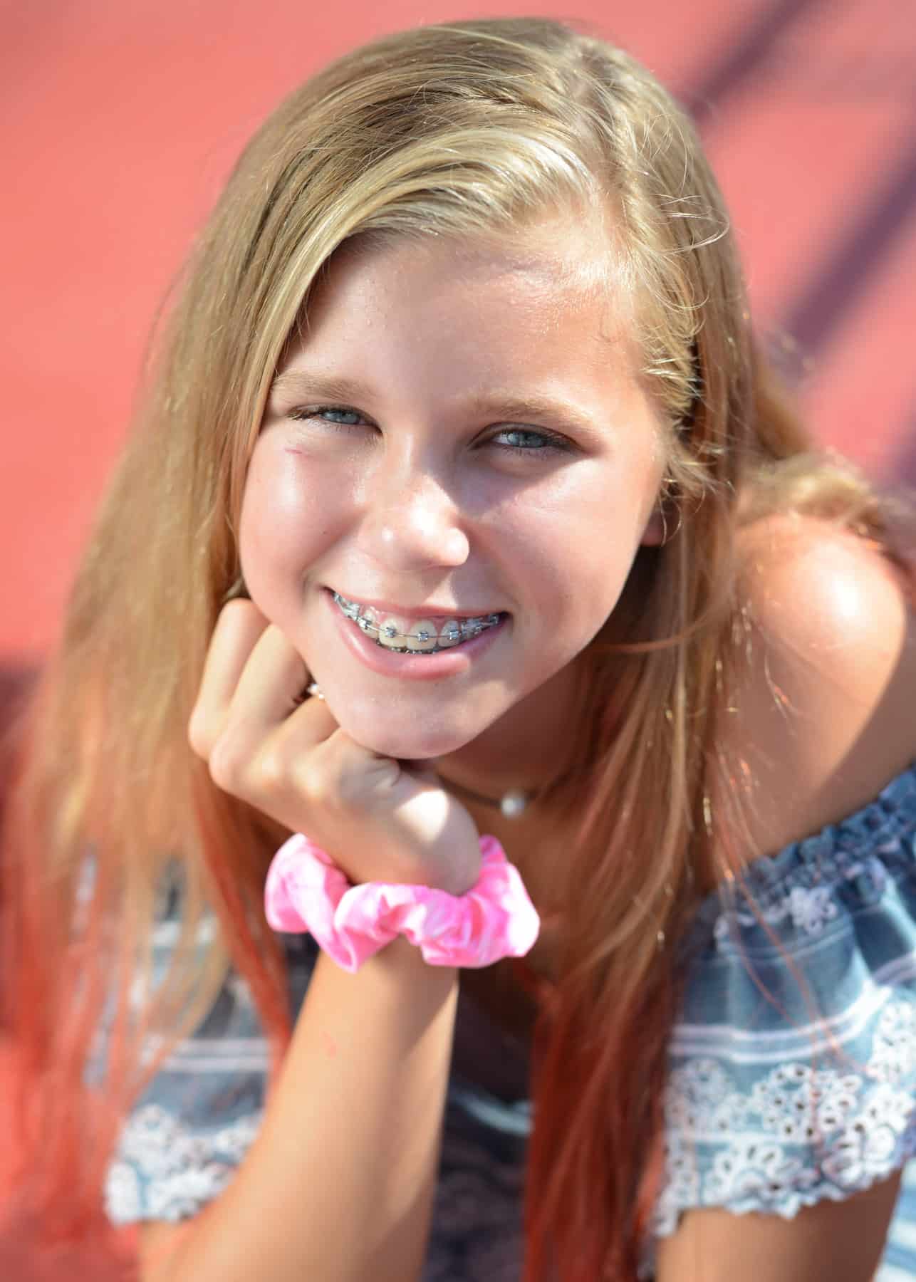 A blonde teenage girl smiling with braces on.