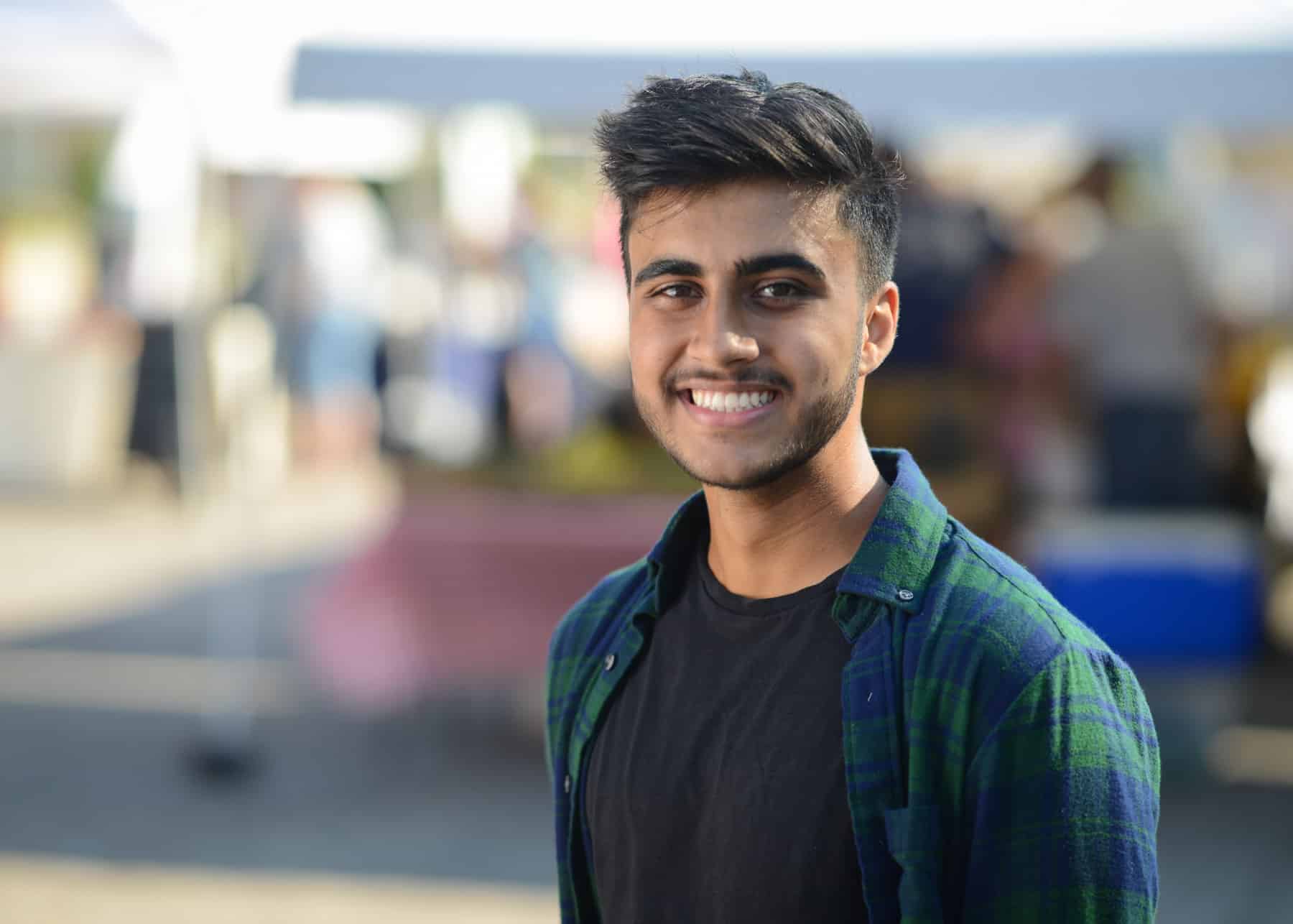 A smiling teen boy with black hair and a plaid t-shirt.