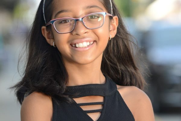 A young smiling girl with dark down hair, glasses and a black blouse.