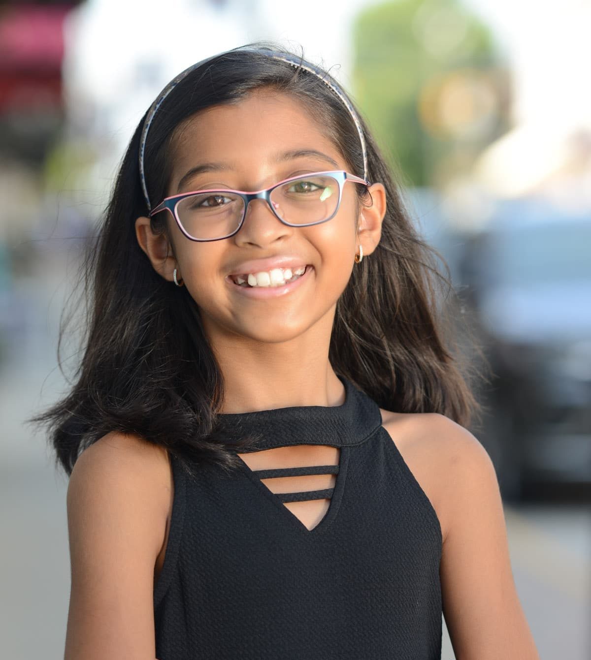 A young smiling girl with dark down hair, glasses and a black blouse.