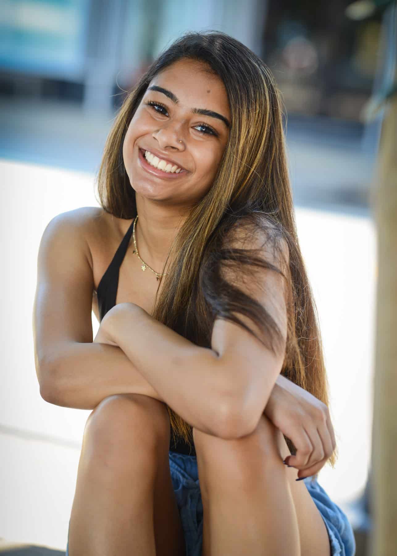 Teen girl with brown hair sitting and smiling outside.