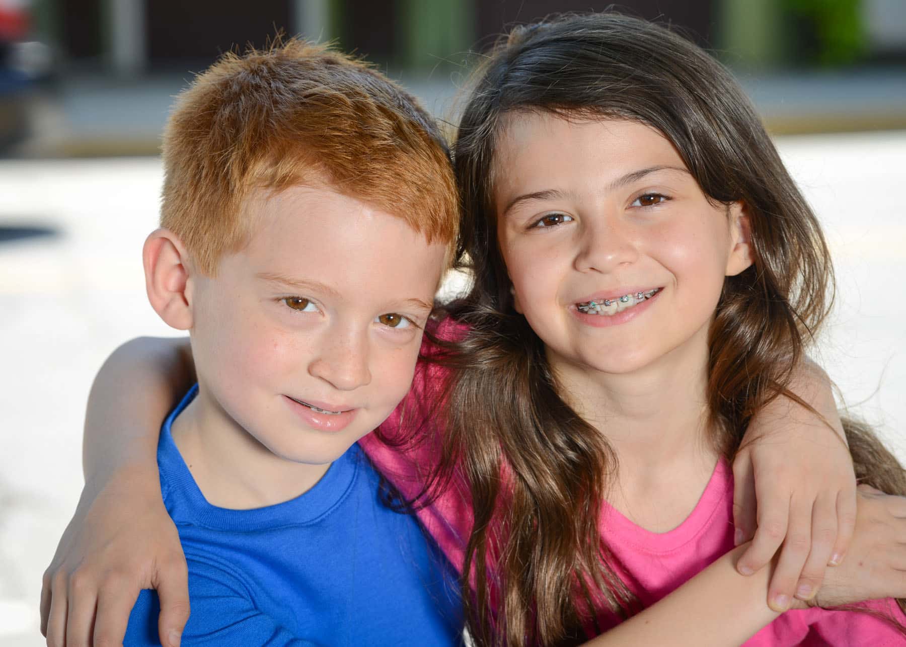 A young boy with red hair and braces embracing a young girl with brown hair and braces.