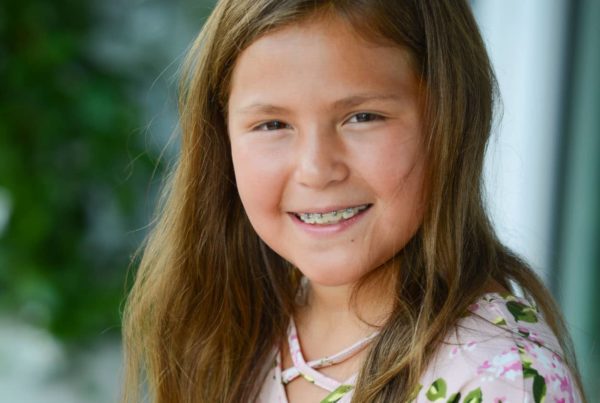 A young girl with a floral shirt and brown hair and braces.