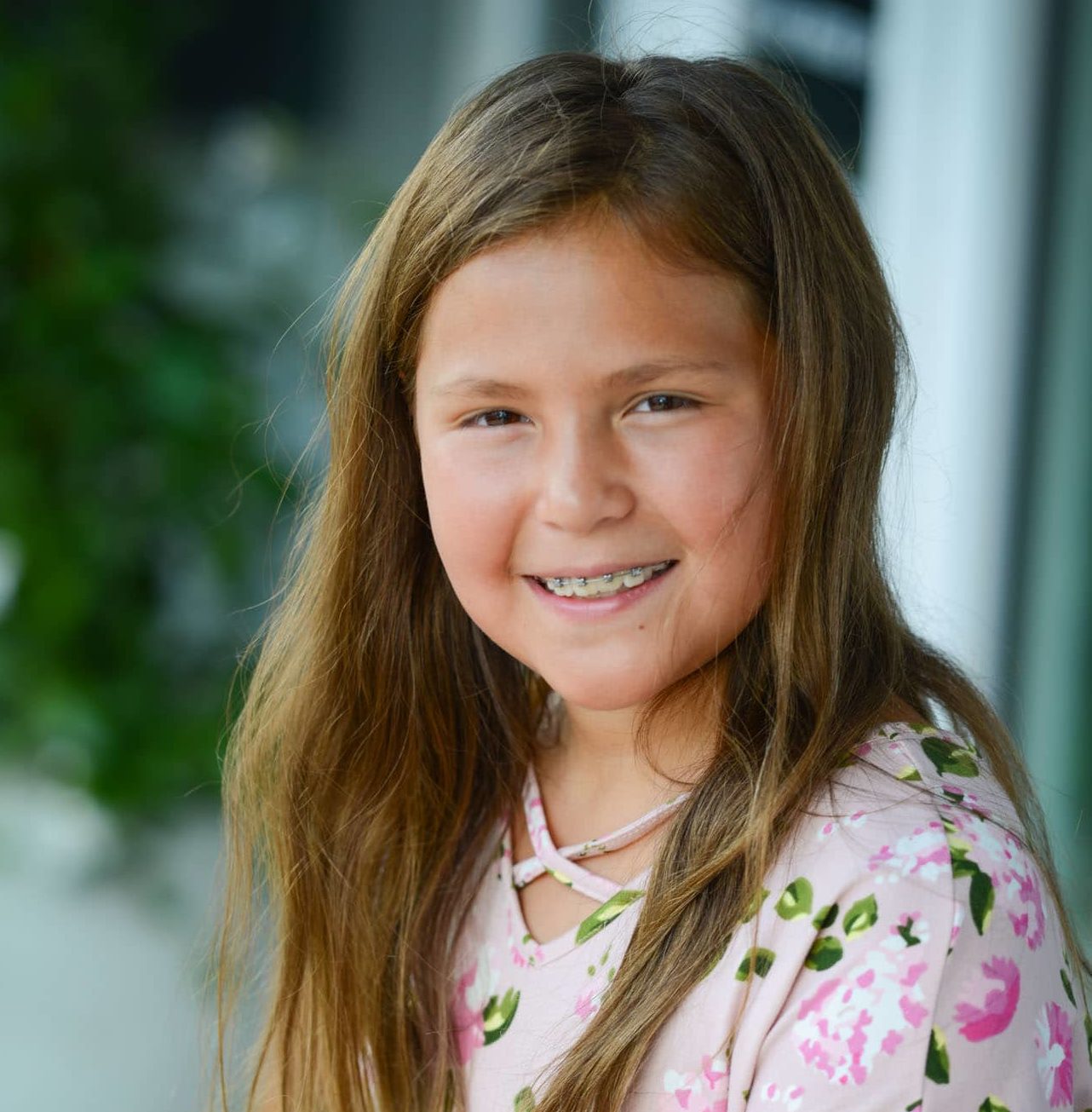 A young girl with a floral shirt and brown hair and braces.