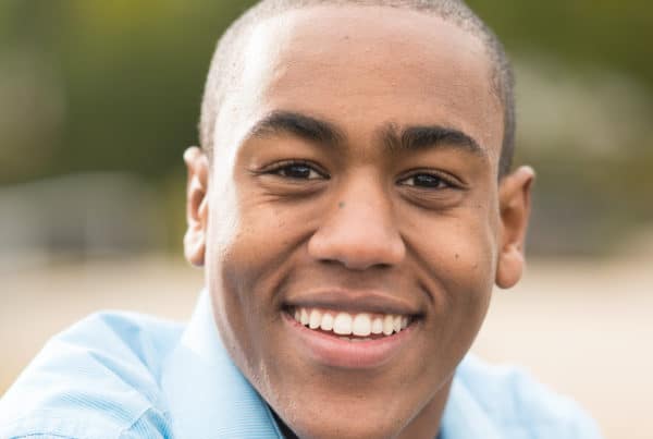 A man with a shaved head smiling in a park.