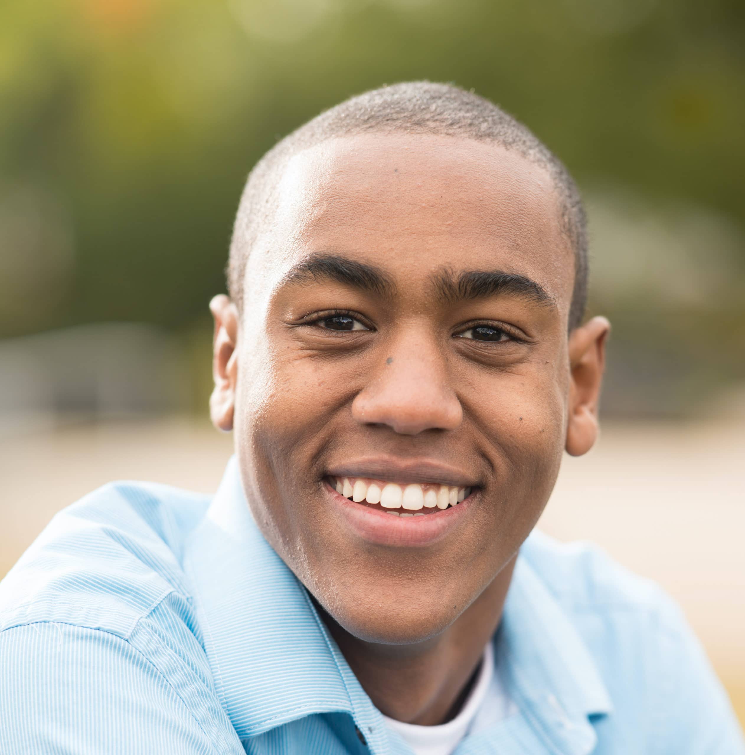 A man with a shaved head smiling in a park.