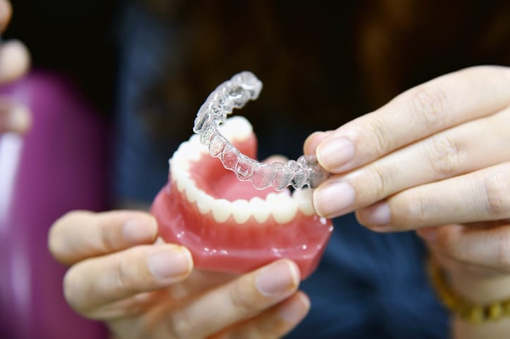 A pair of hands applying a clear aligner to a model of the lower teeth and gums.