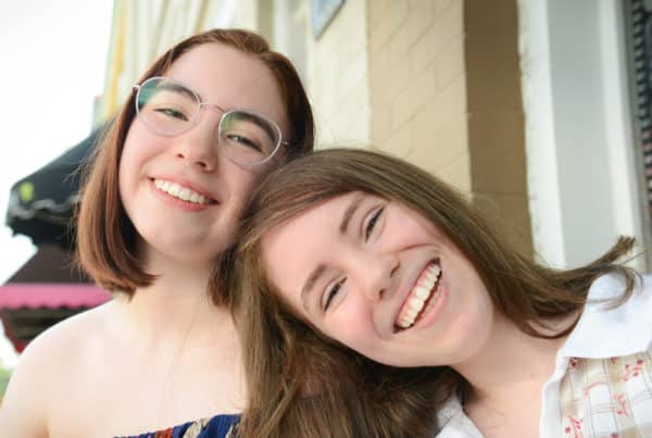 A girl smiling and leaning on her friend's shoulder.