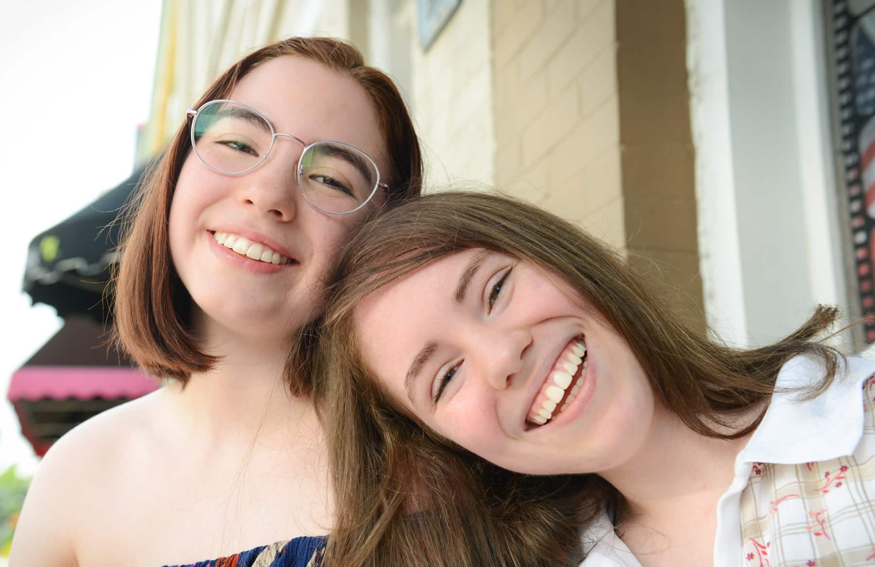 A girl smiling and leaning on her friend's shoulder.