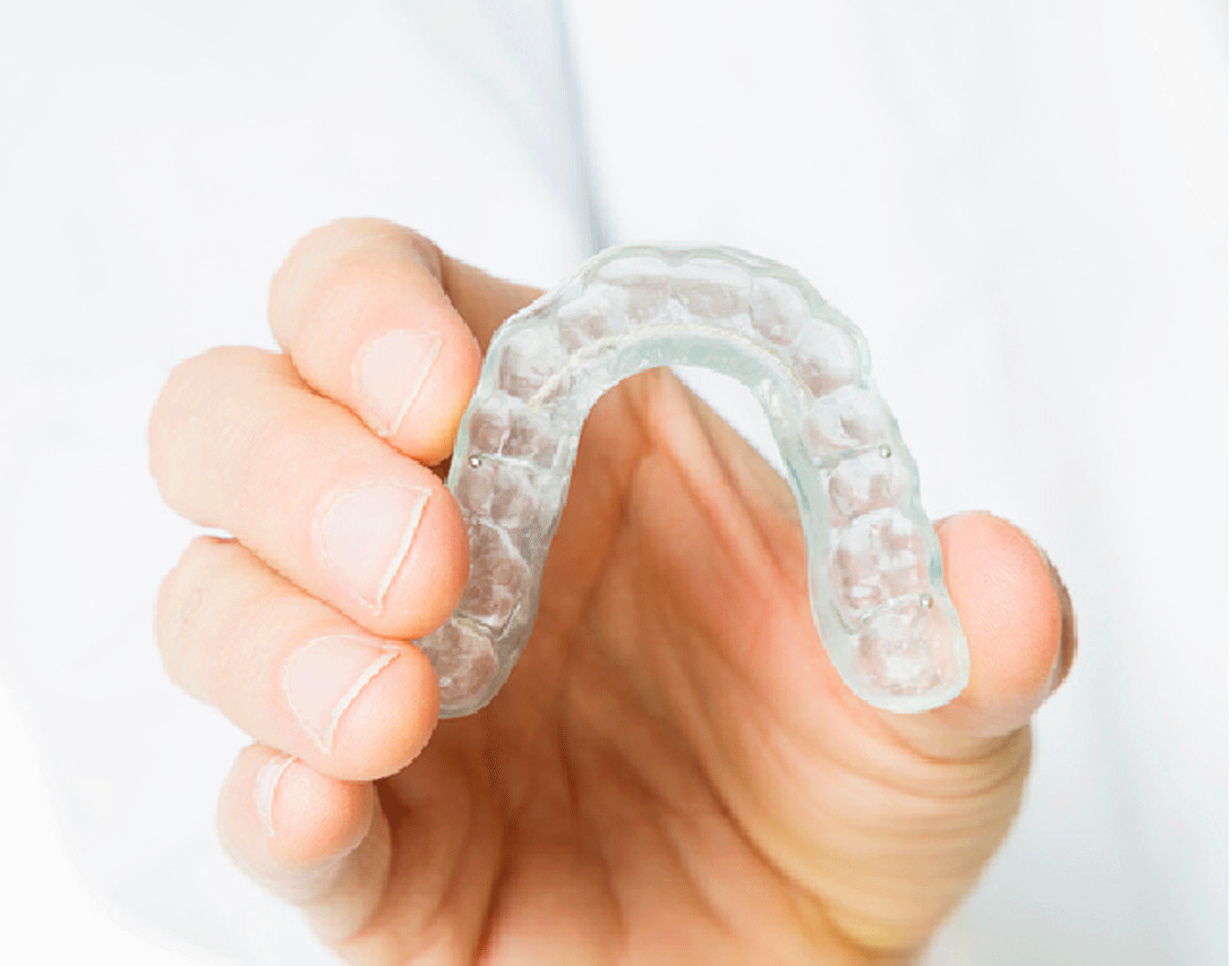 A hand holding up a clear aligner tray.