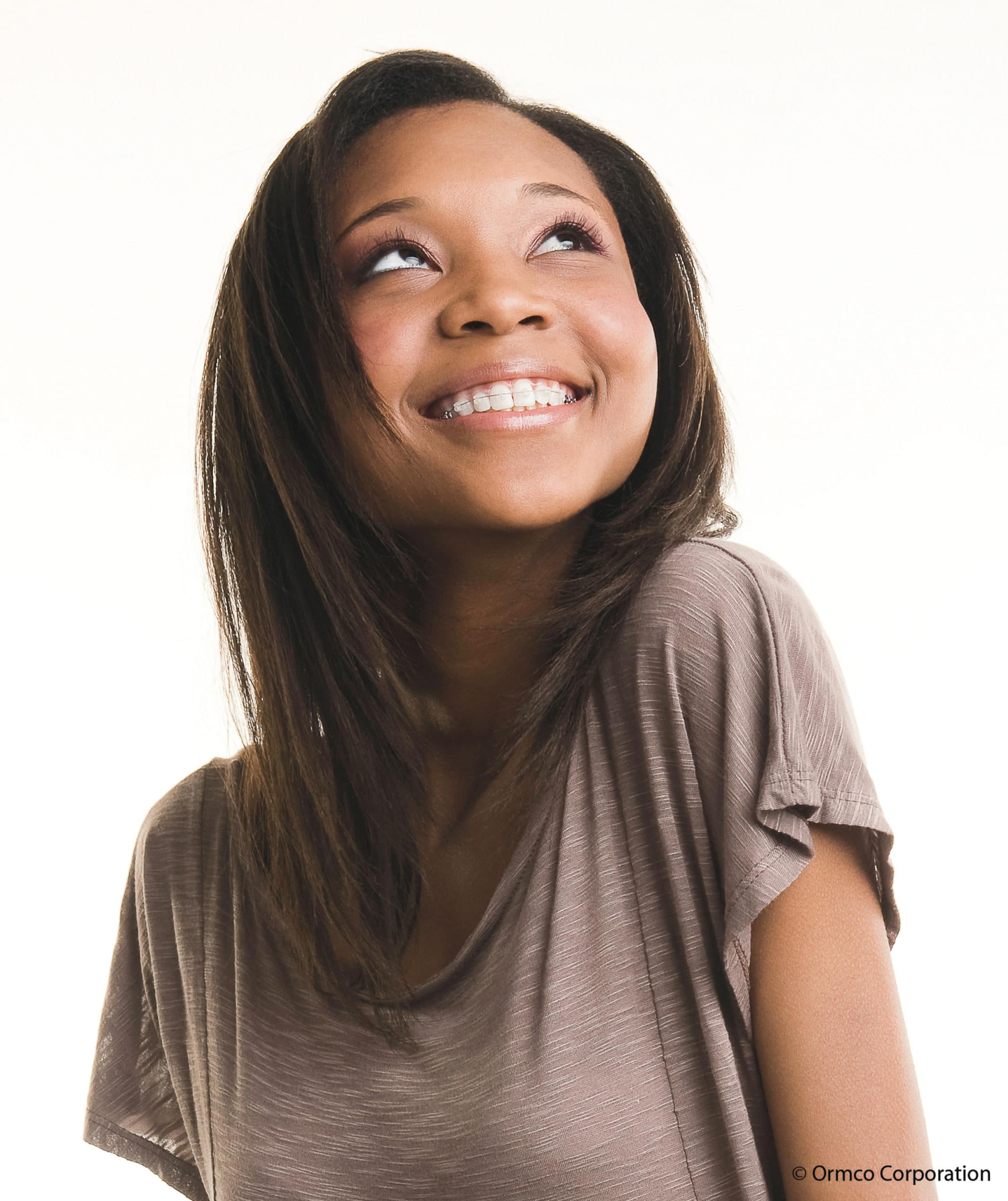 A teenage girl with brown hair smiling with clear braces on.