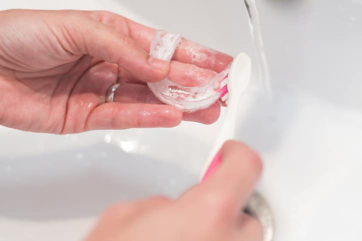 A pair of hands using a toothbrush to clean a clear aligner tray.