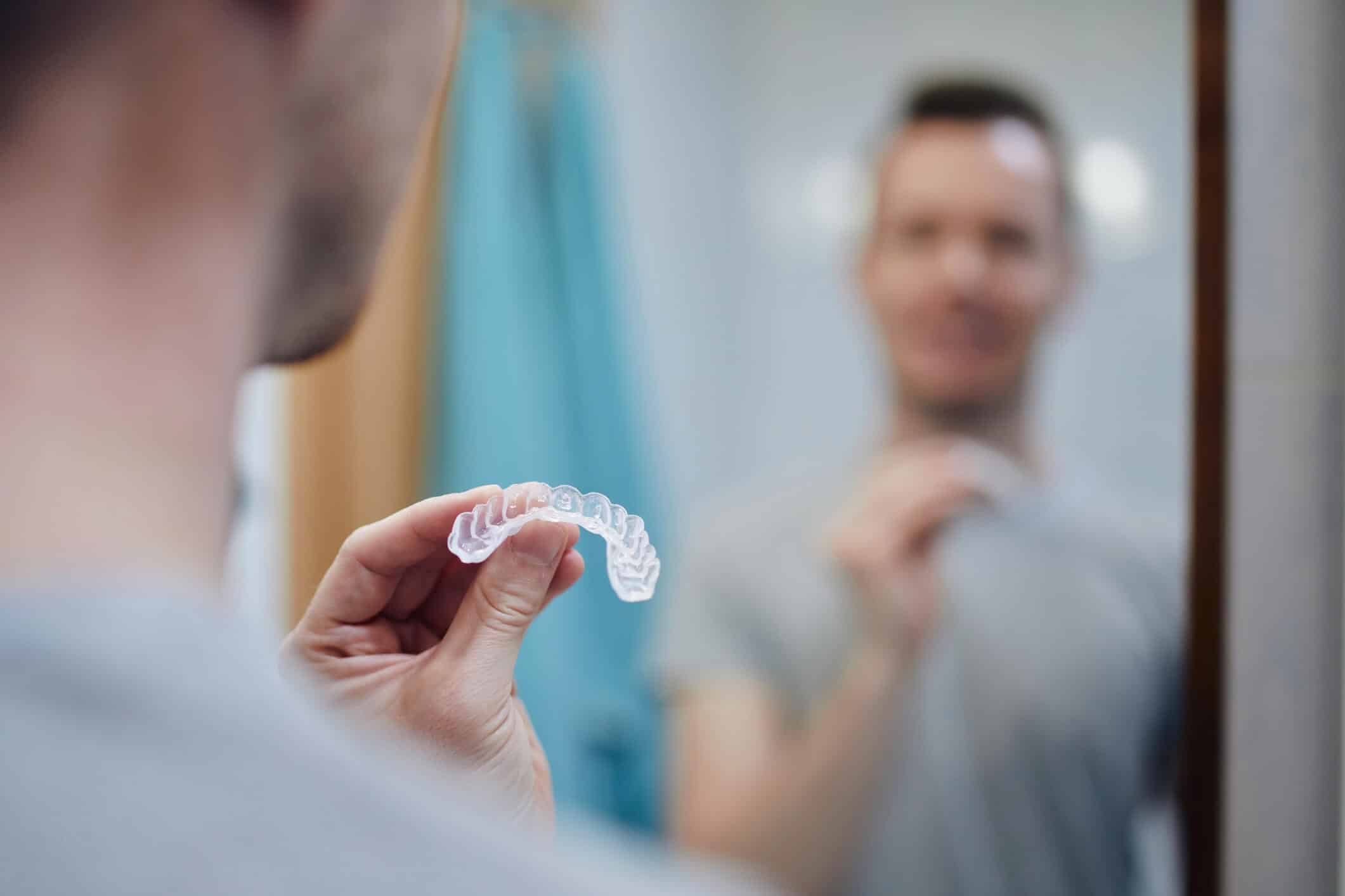 Close up of a man applying his aligners while looking in a mirror.