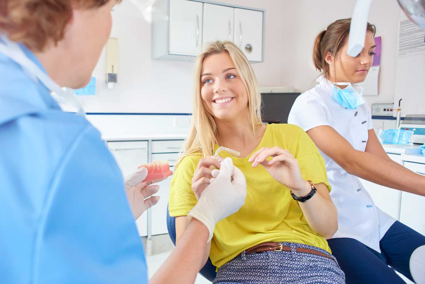 An orthodontist showing a teen girl how to apply clear aligners to a model of bottom teeth.