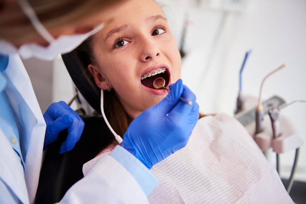 Orthodontist with a mask examining a girl's braces with a dental mirror.