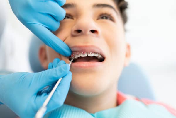 An orthodontist working on a teen boy's pink braces.