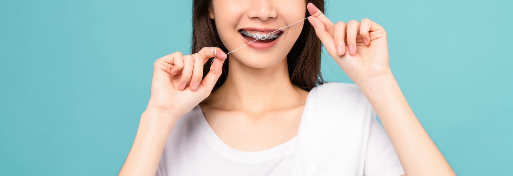 Smiling woman cleaning braces on teeth with dental floss on blue background, Concept oral hygiene.