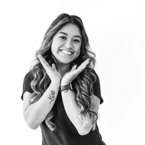 curly haired orthodontic assistant smiling while making a v shape with her hands under her chin.