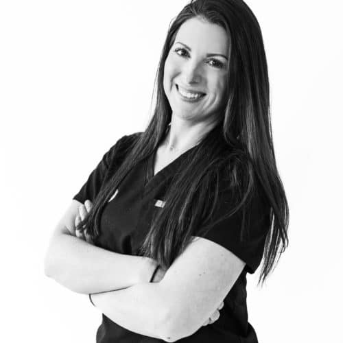 an orthodontic assistant in black scrubs smiling at the camera with her arms crossed in front of her.