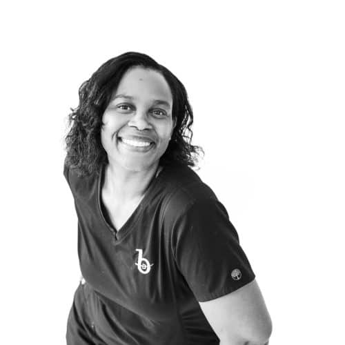 orthodontic assistant in scrubs leaning forward with her hands on her hips and smiling at camera.