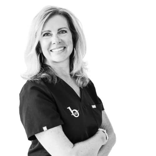 a blonde woman wearing black scrubs while smiling at the camera and crossing her arms.