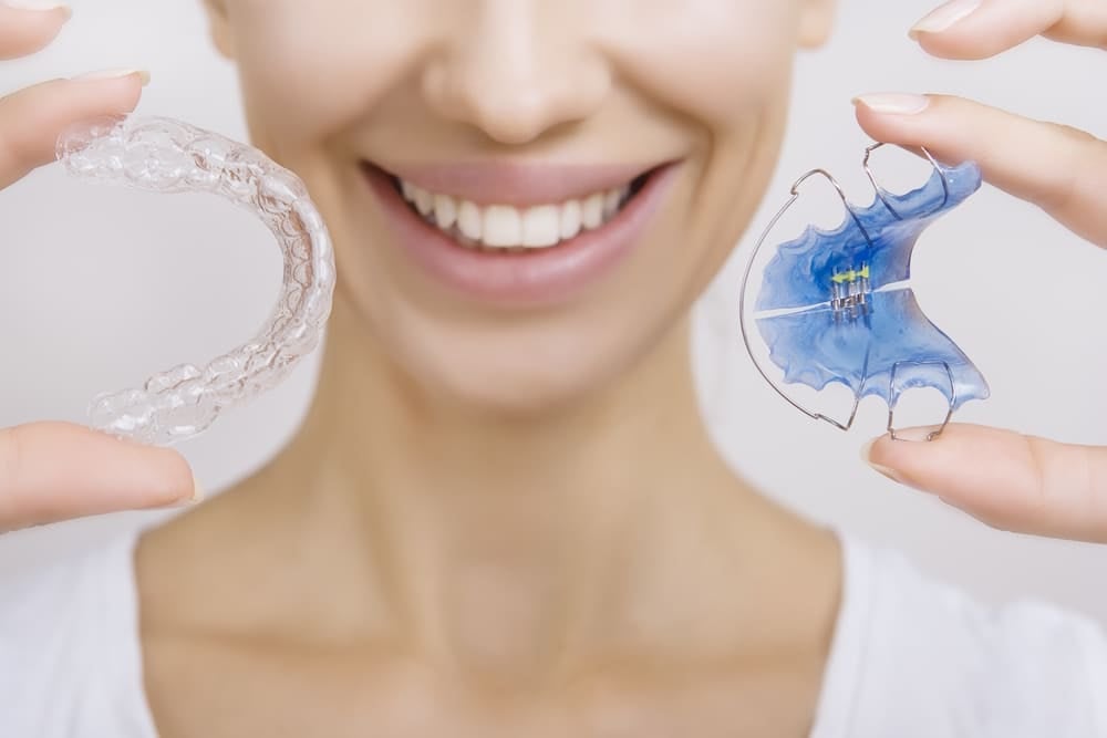 Beautiful smiling girl holding retainer for teeth